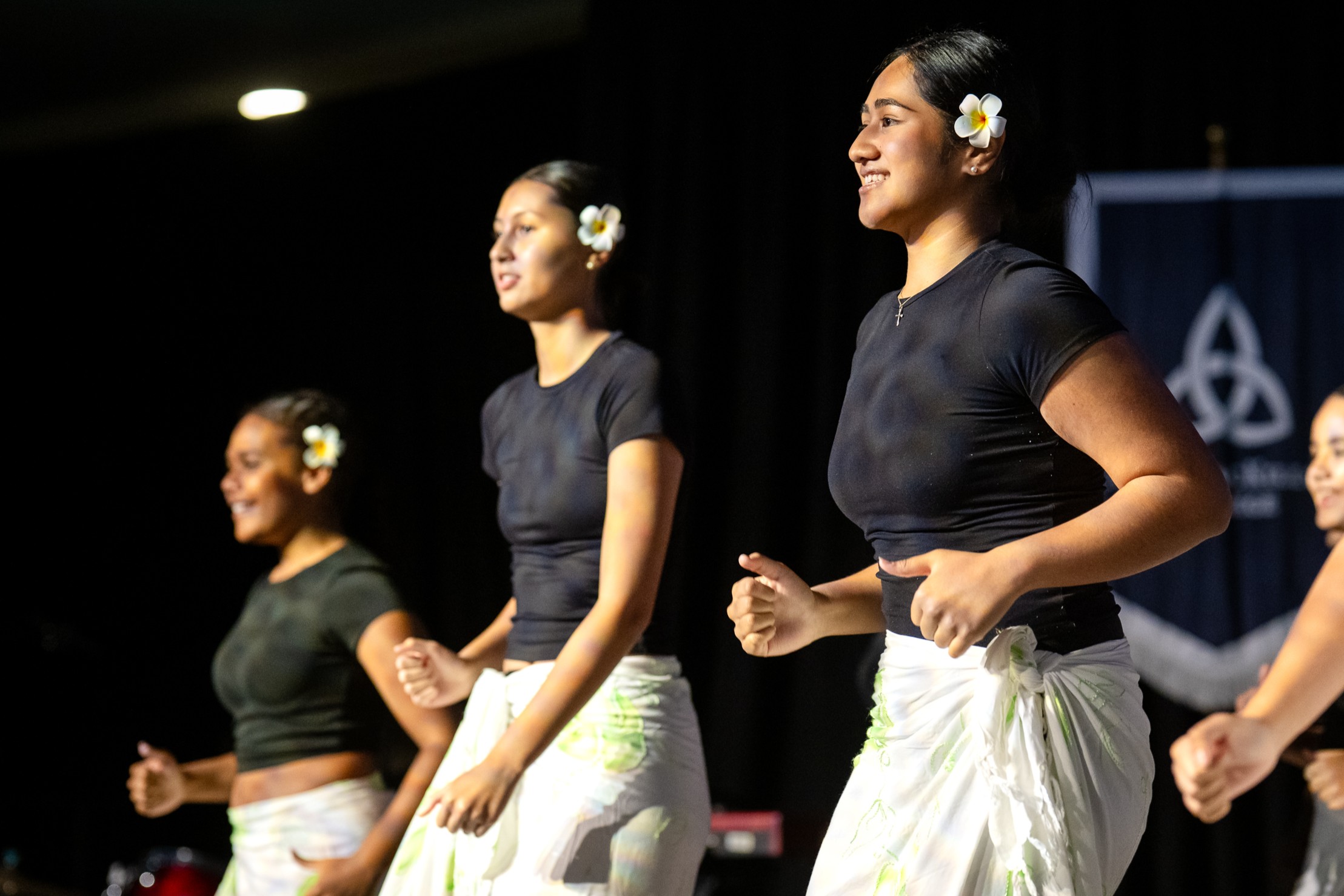 Students performing a cultural dance on stage wearing coordinated outfits with flowers in their hair