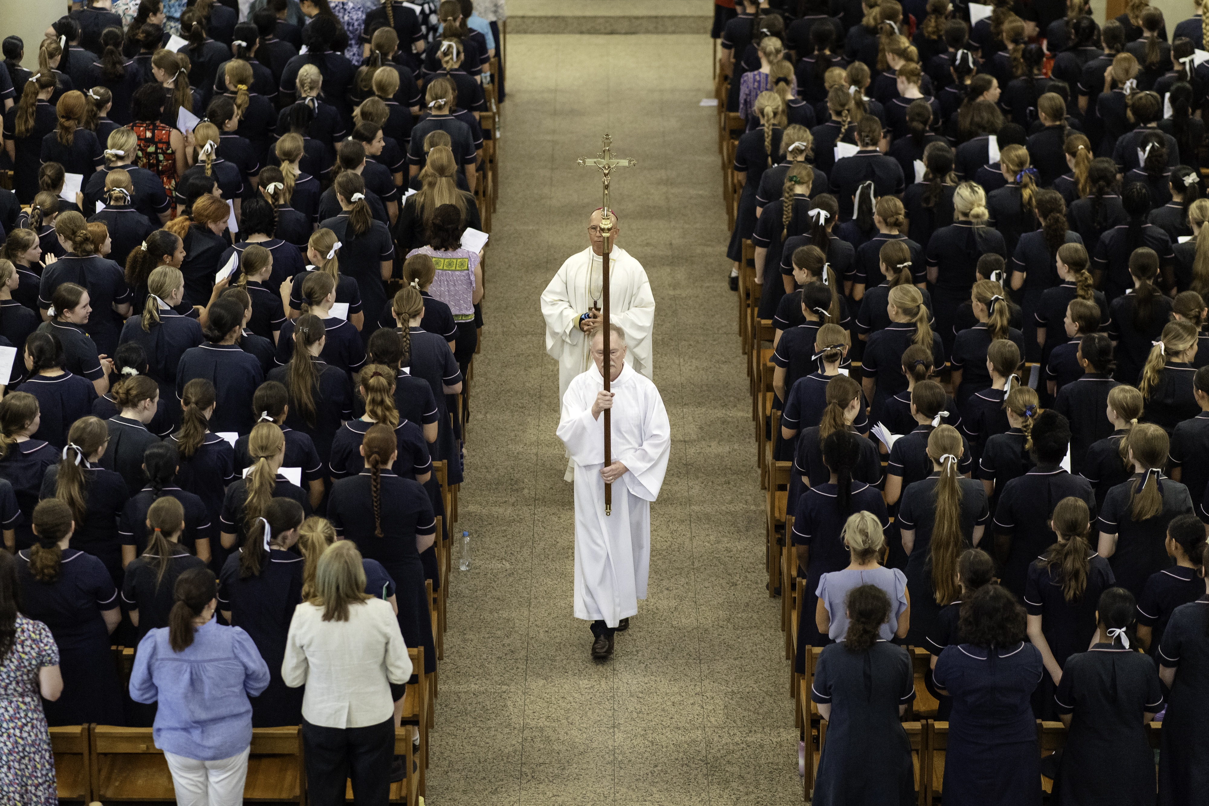 MMC Opening Mass Religious procession moving down the central aisle of a church surrounded by students standing in pews