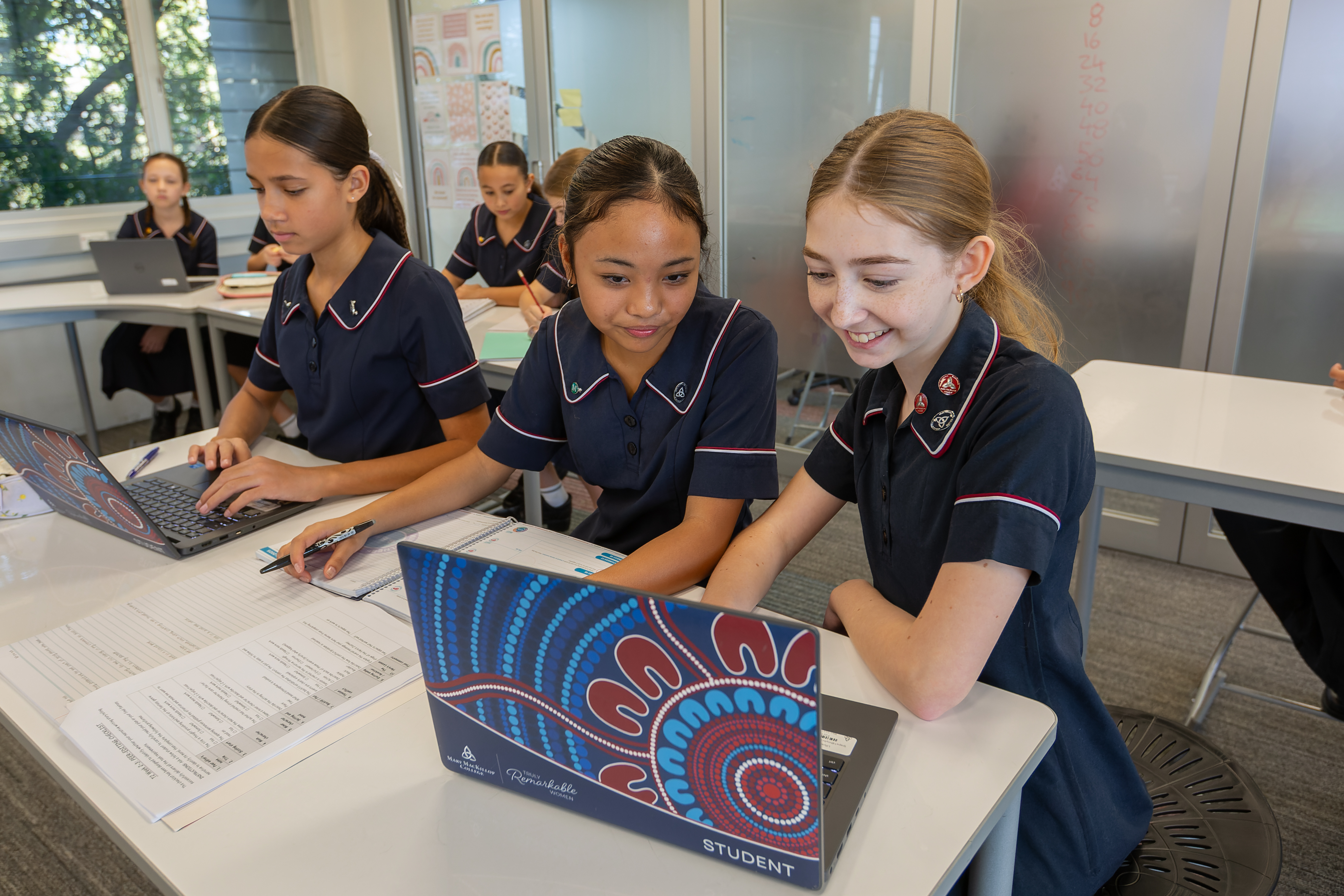 Students in school uniforms working together on laptops at classroom desks