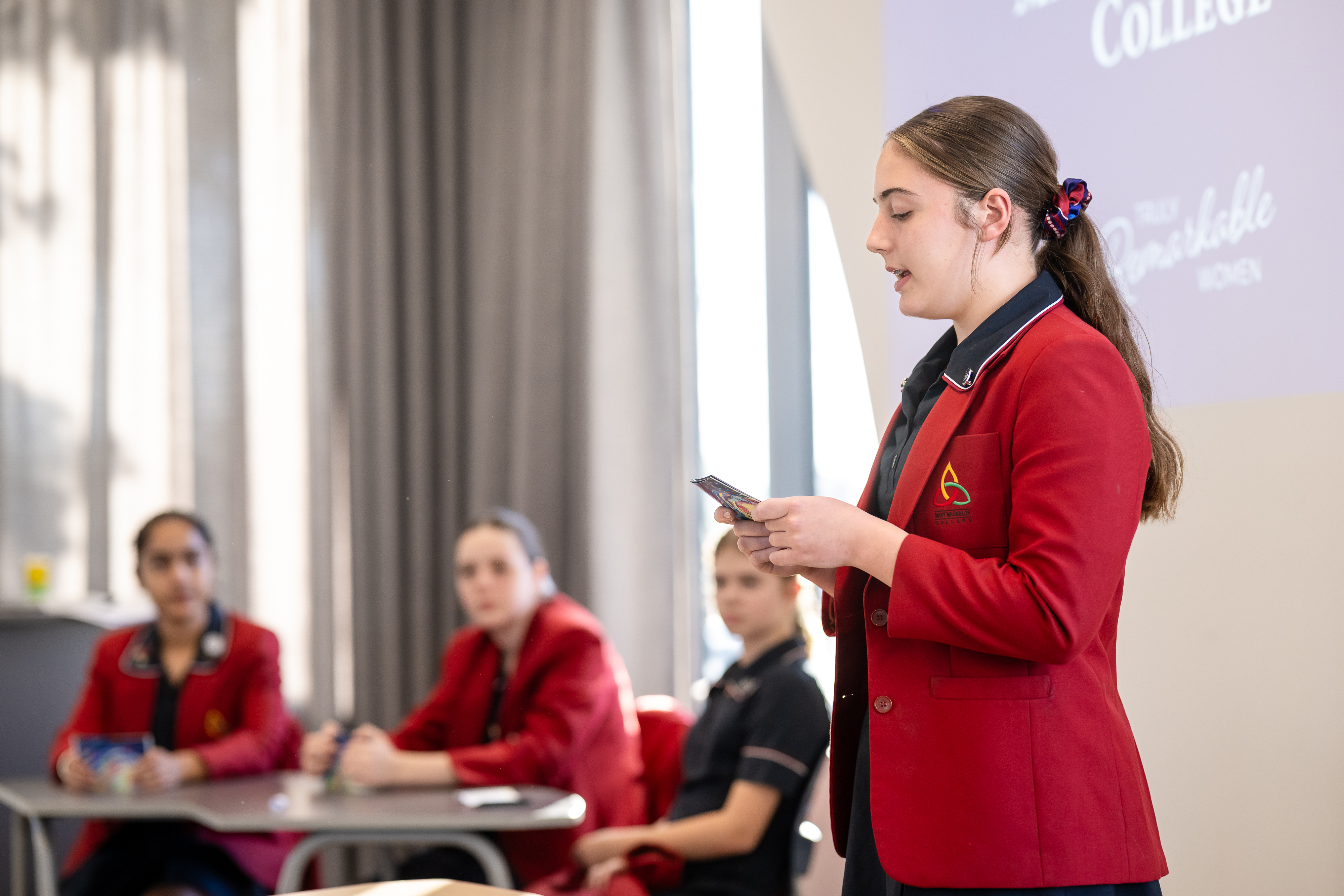 Student in school uniform standing and presenting to classmates while holding cue cards