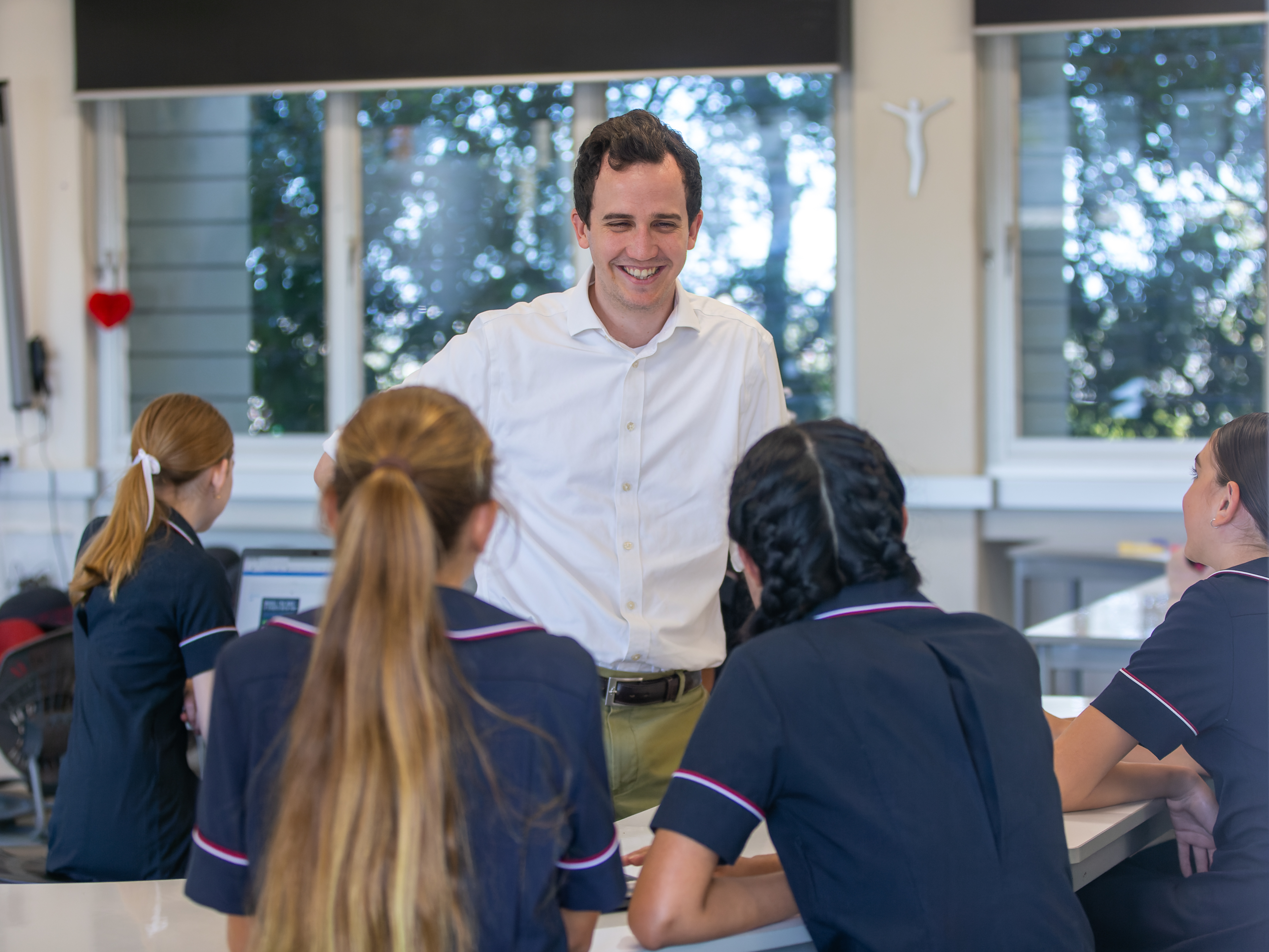 Adult standing and talking with students seated at desks in a classroom