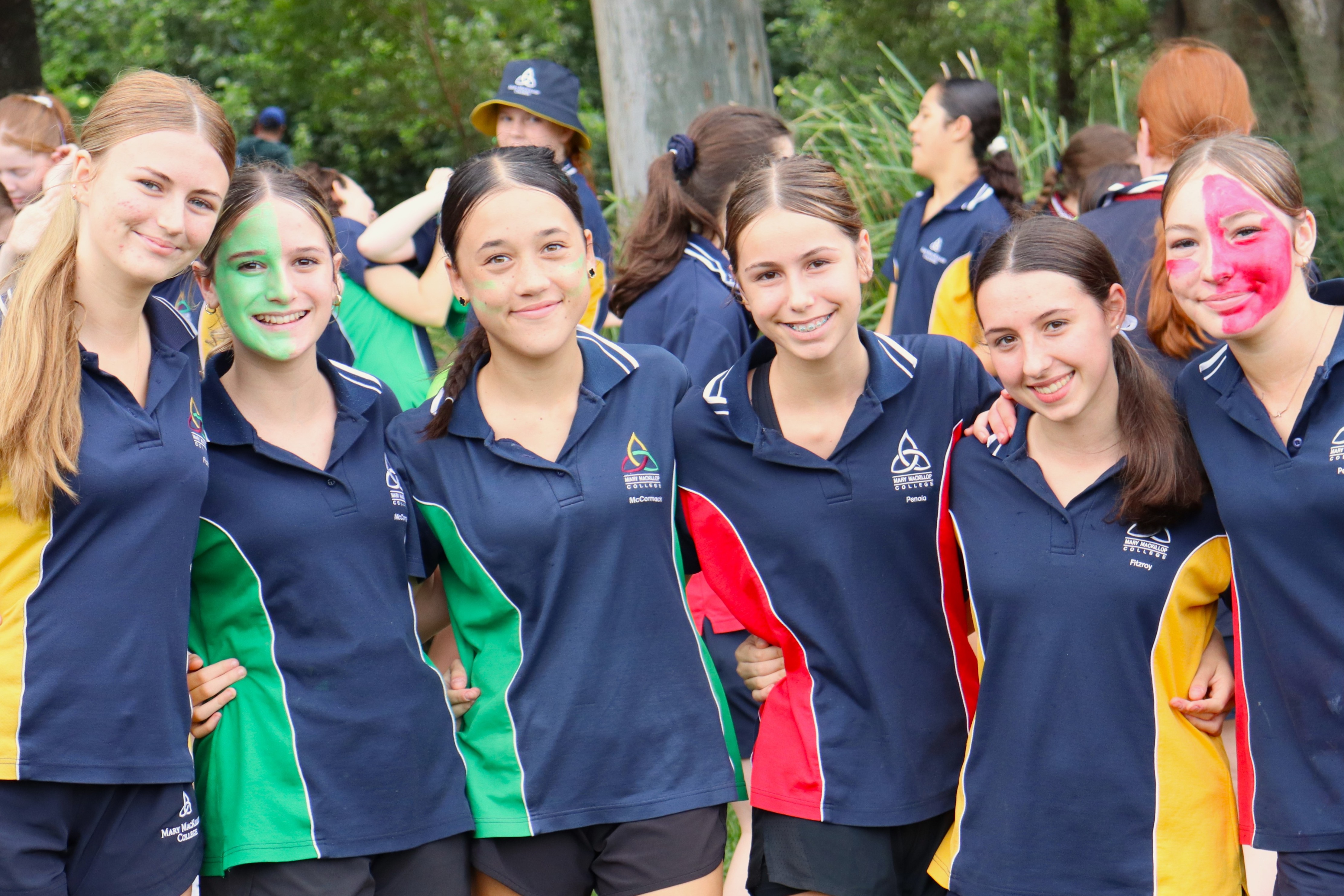 Group of students in school uniforms standing together outdoors with coloured face paint during a school event