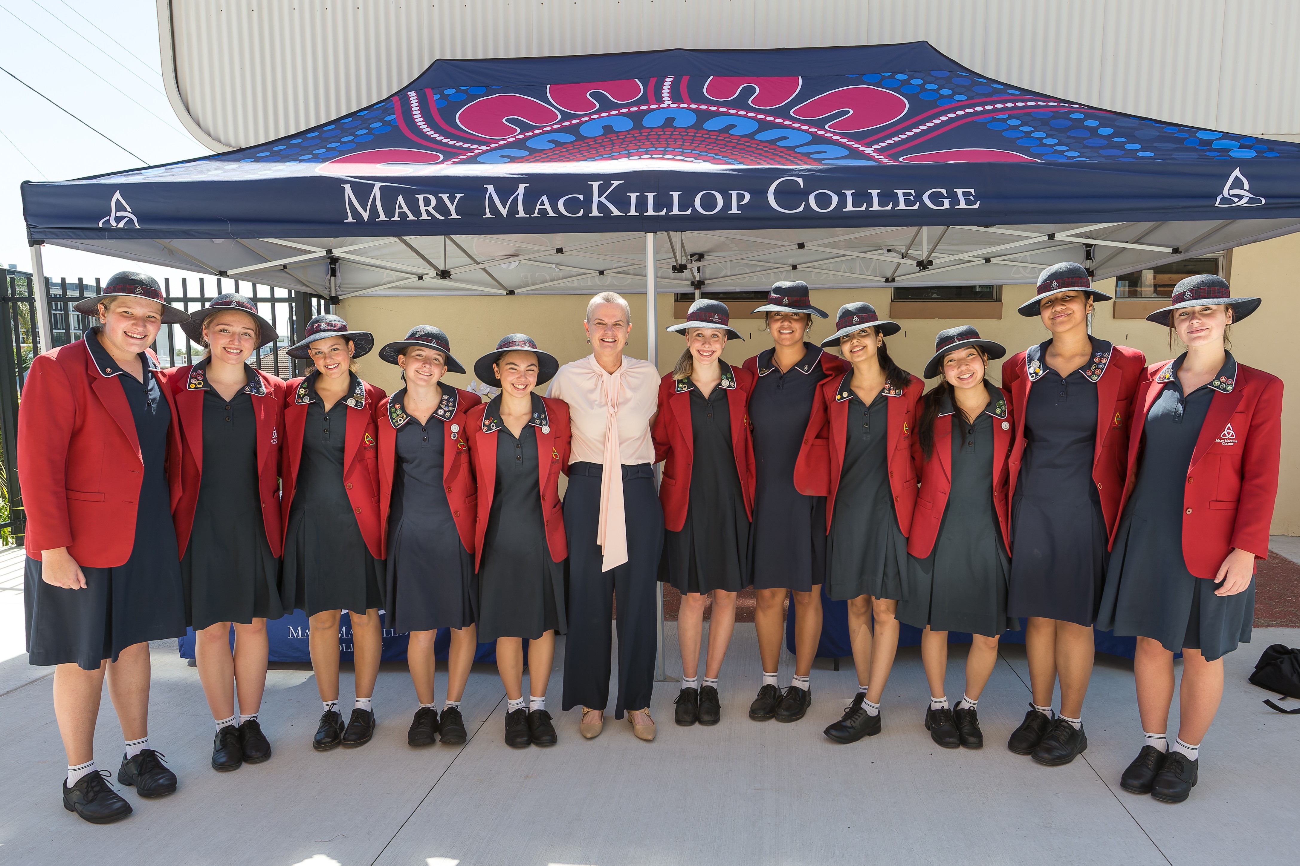 Group of students and an adult standing together under a Mary MacKillop College marquee outdoors
