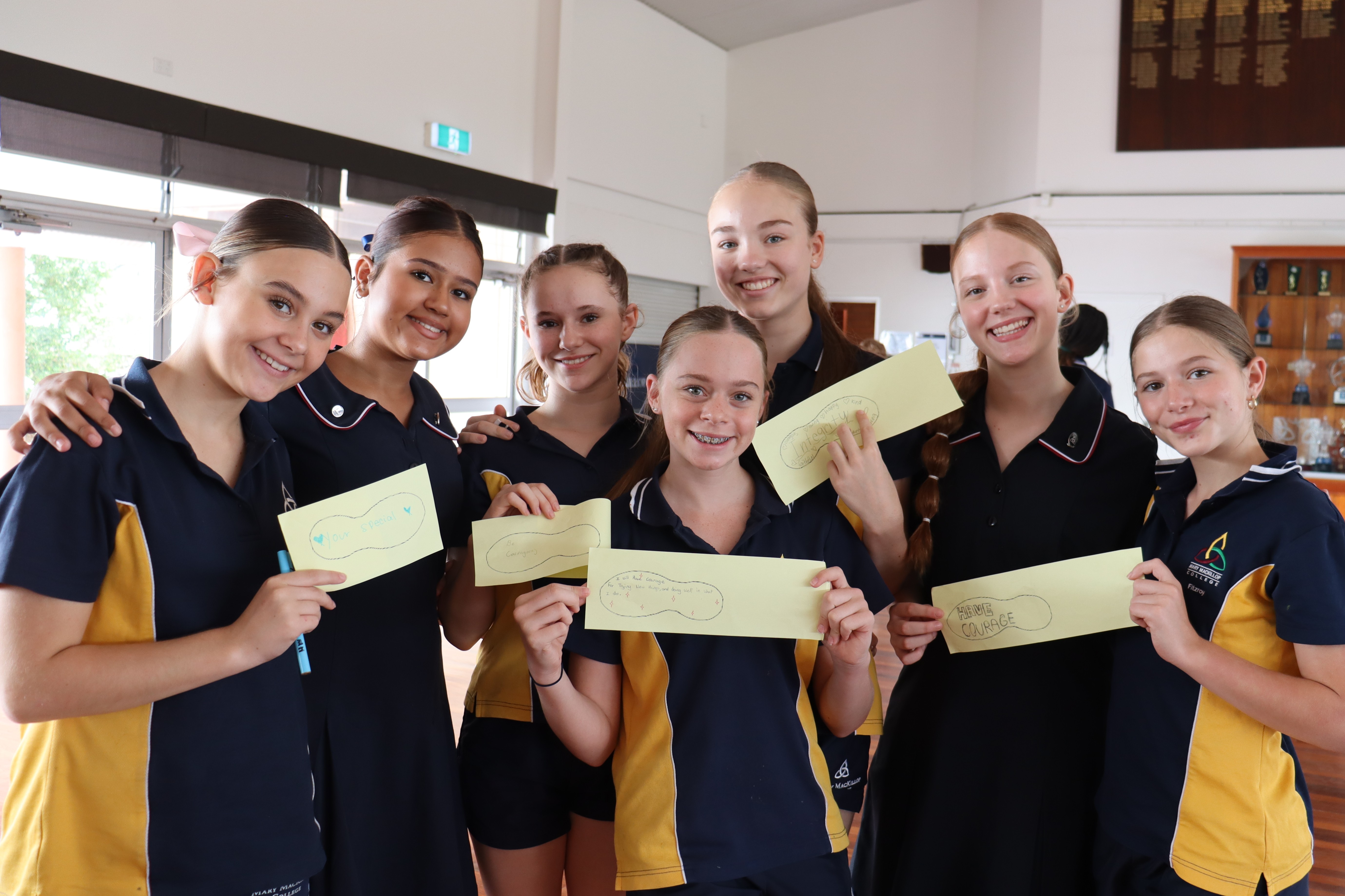 Group of students in school uniforms standing together indoors holding handwritten notes