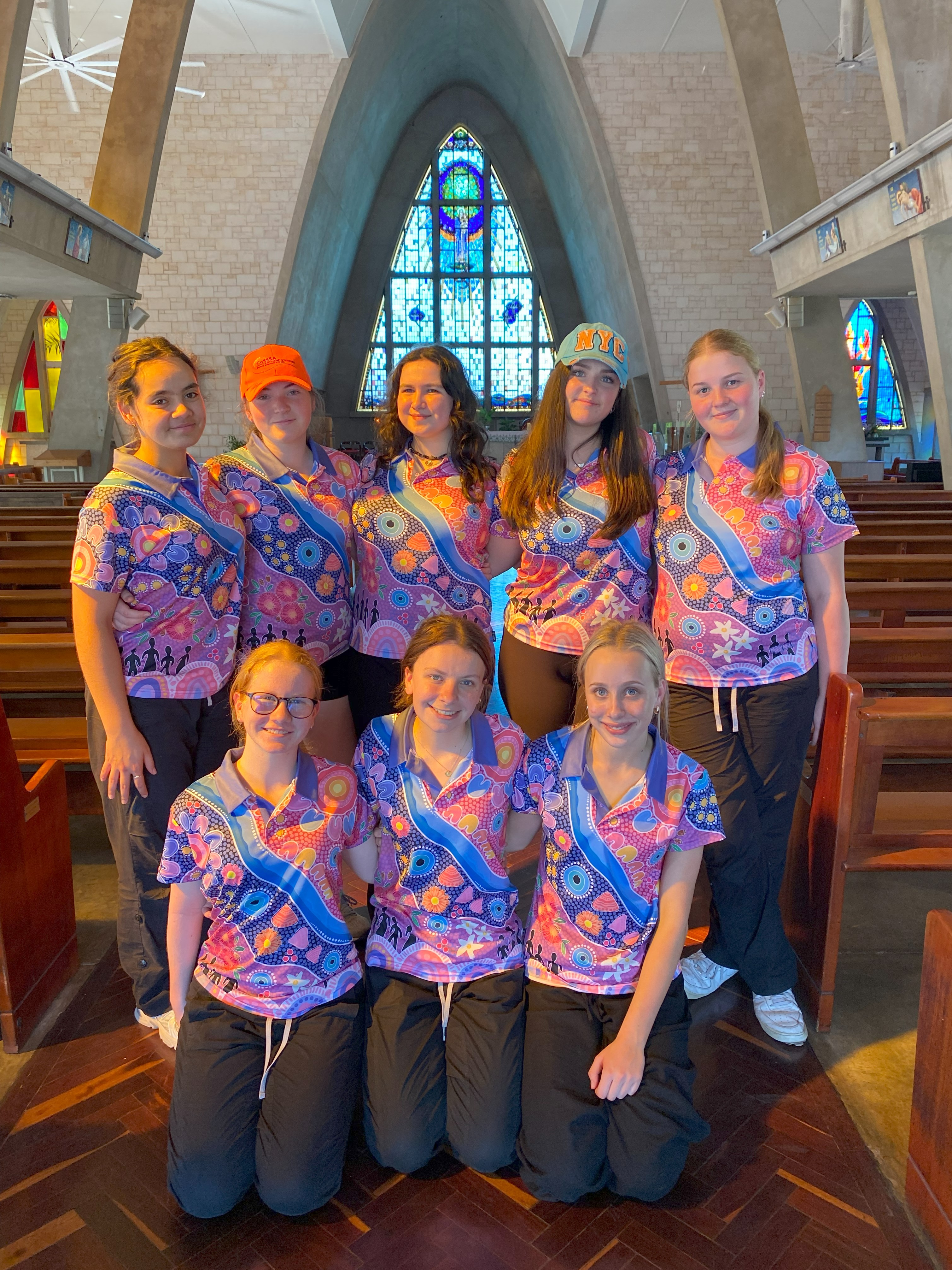 Group of students wearing patterned shirts standing together inside a church with stained glass windows