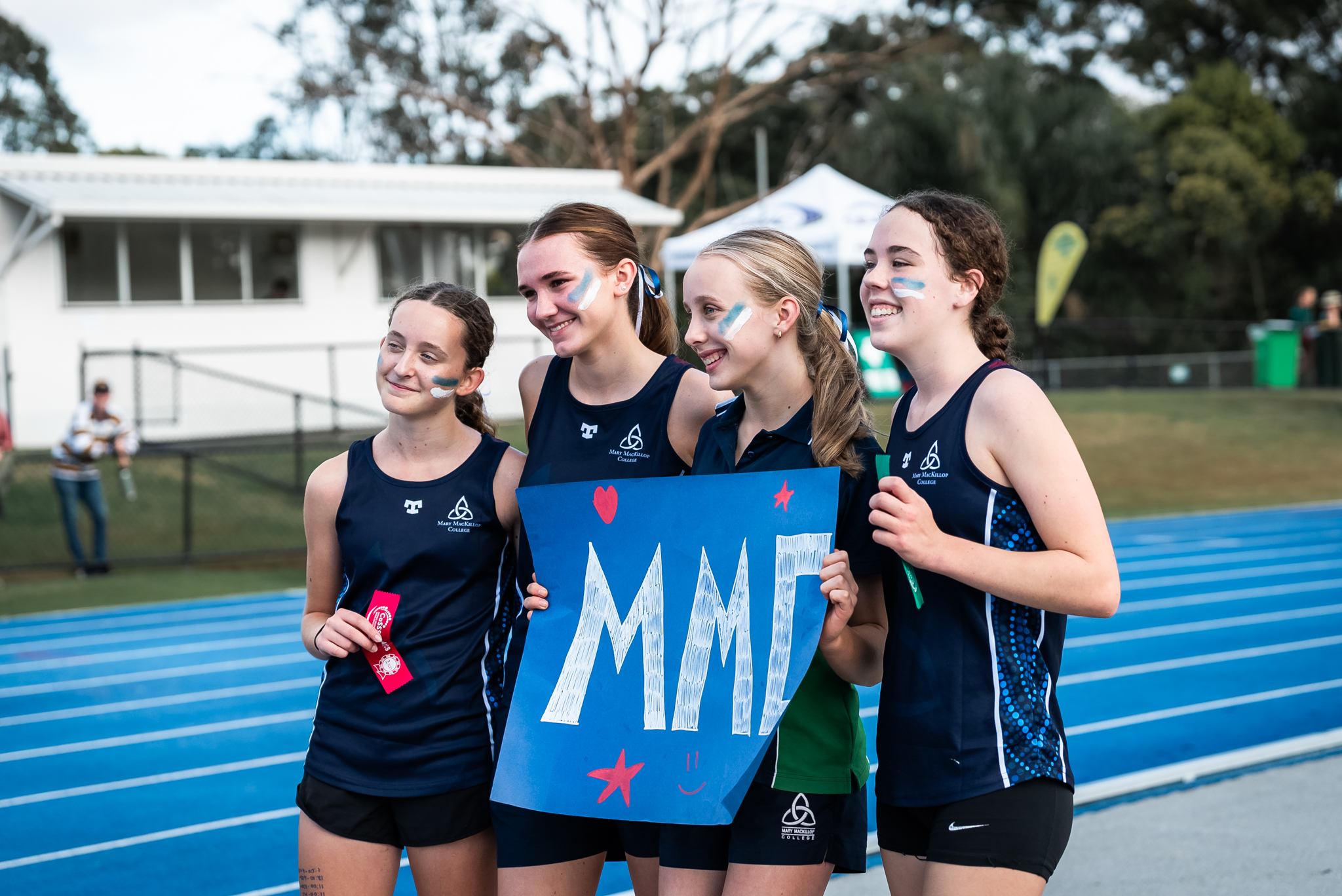 Students in school sports uniforms standing on a running track holding a handmade sign together