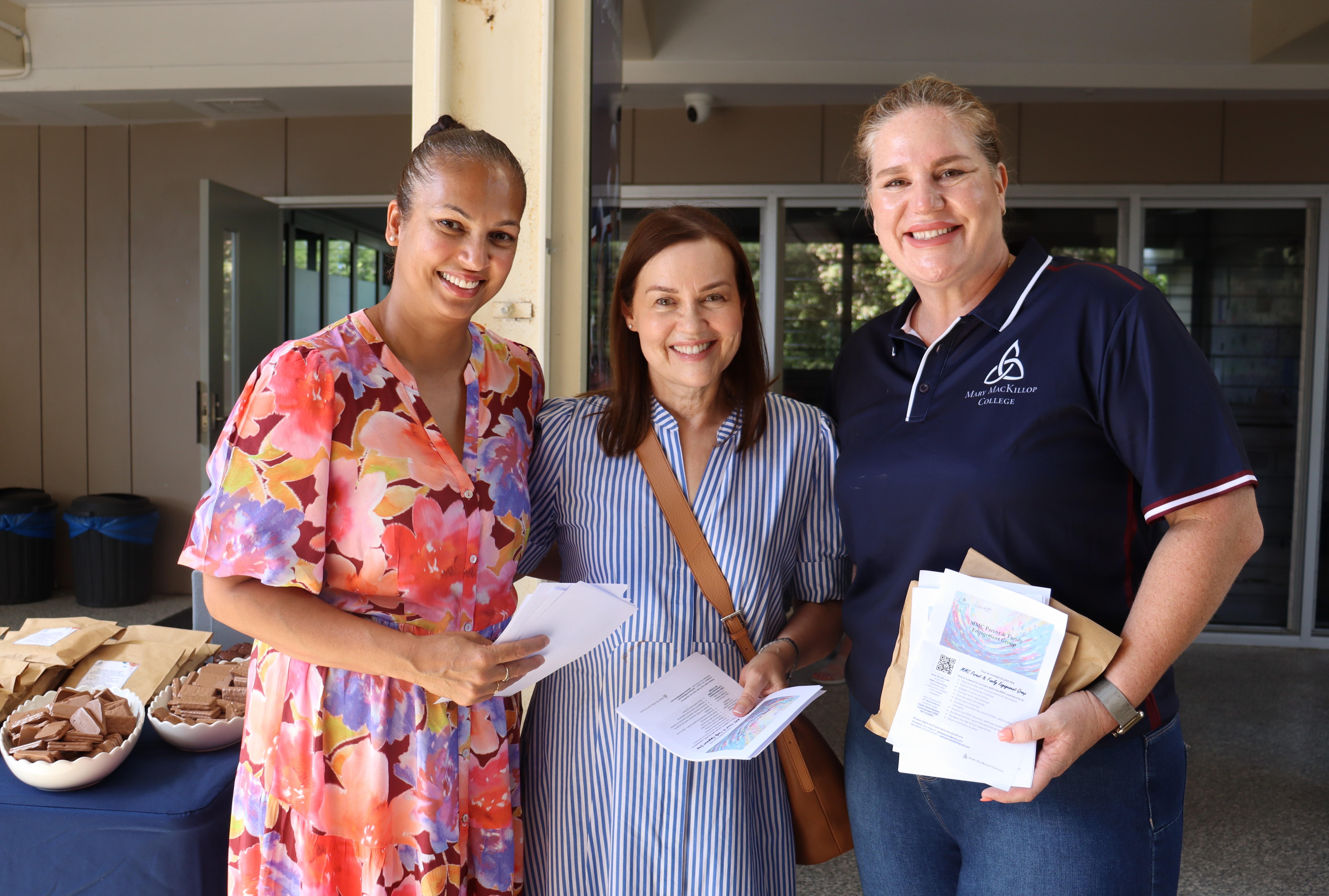 Three adults standing together outdoors holding papers near a table with food items
