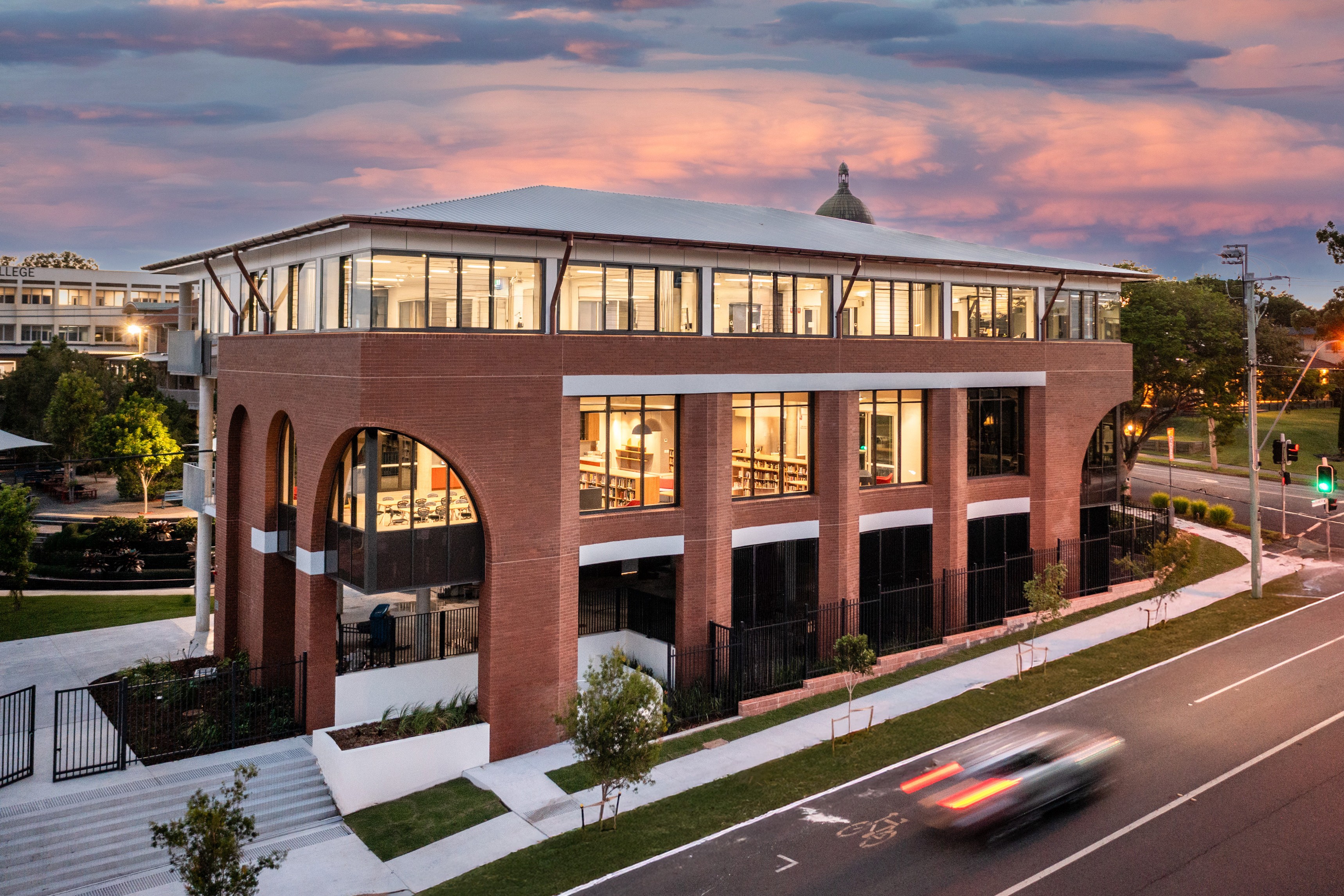 Modern multi‑storey school building with brick arches and large windows at dusk