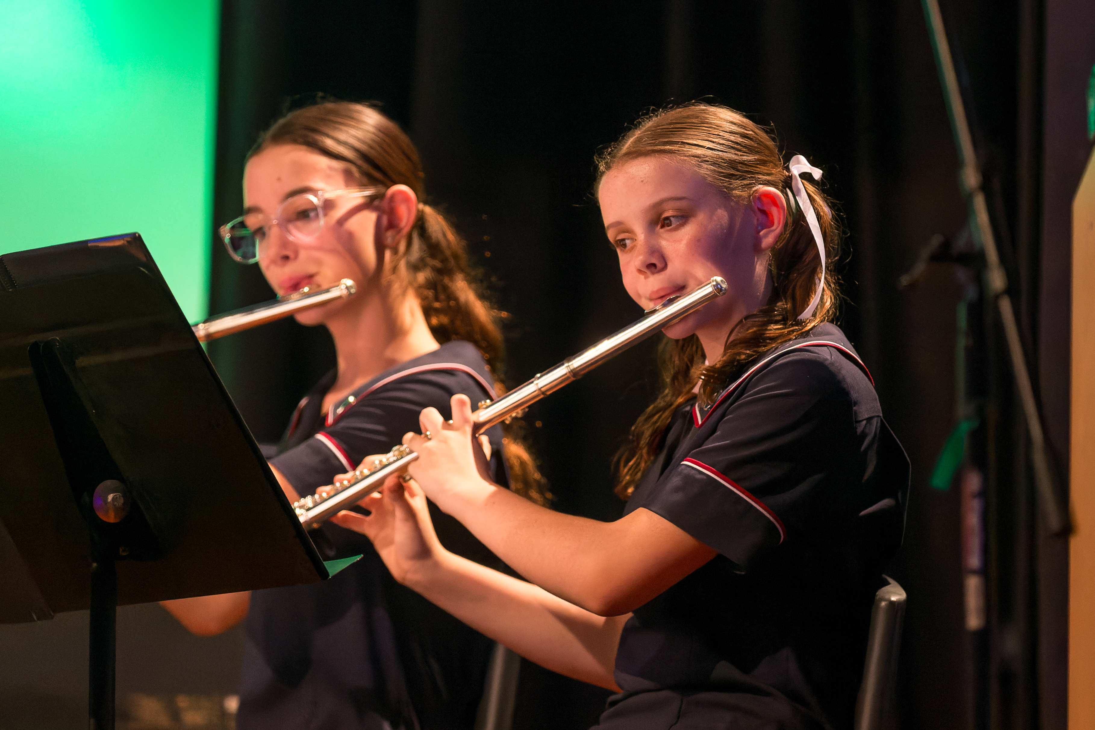 Two students in school uniforms playing flutes on stage during a music performance