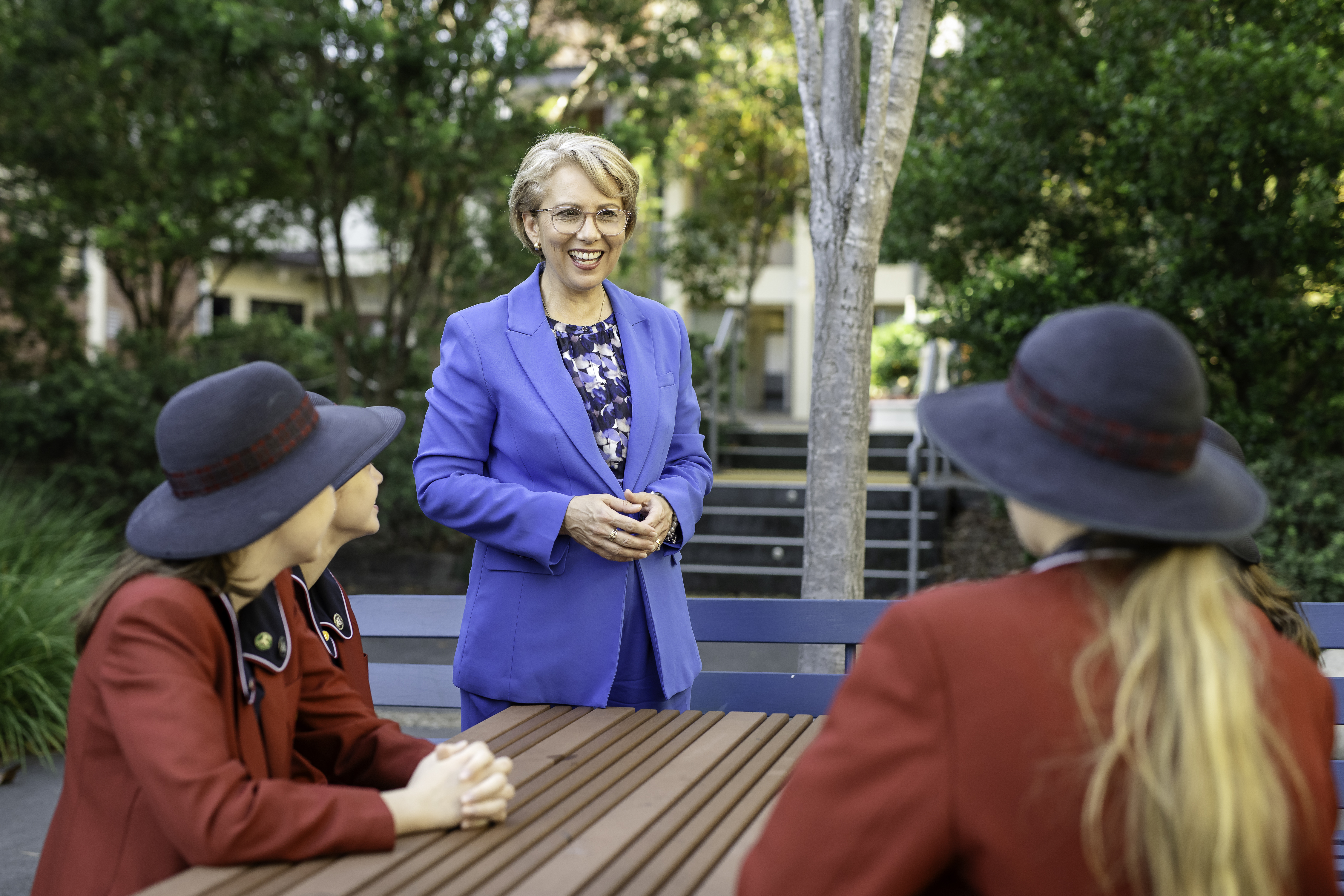 Erin Wedge College Principal standing outdoors speaking with students seated at a table on school grounds